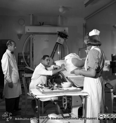 Göran Bauer förbereder en myelografi. 
Pärm äldre neg. 1951-1958, från fotograf Björn Henrikssons samling. Omärkt bild. Troligen röntgenläkare Oliver Axén som tittar på. Negativ
Nyckelord: 1950-talet;MAS;Malmö;Ortopedi;Röntgen