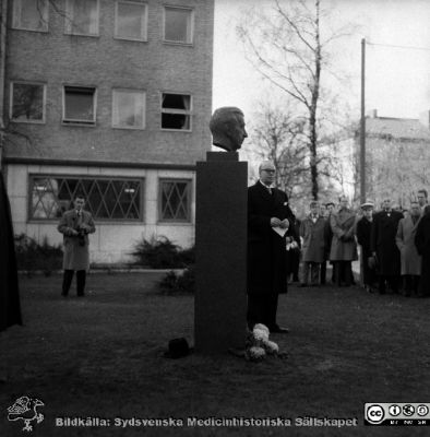 Avtäckning av byst av Fritz Bauer på Malmö Allmänna sjukhus 1957
Pärm äldre neg. 1951-1958 MAS, från fotograf Björn Henrikssons samling.	Påskrift: "MAS, 100 år, 8/11-57". Bysten av Fritz Bauer invigs. Troligen är det Sune Genell som står bakom bysten, med manuskript i handen.
Nyckelord: UMAS;MAS;Malmö_;Jubileum;Byst;Invigning