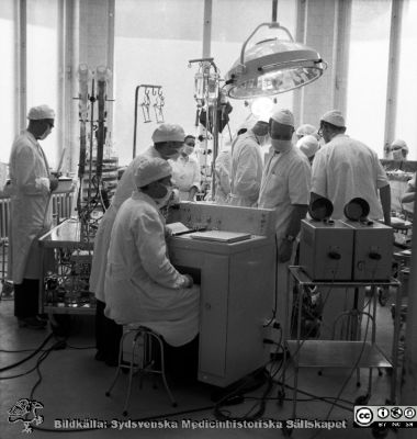 Operation med hjärt-lungmaskin, Malmö 1965
Pärm neg. 1962-1966. Från fotograf Björn Henrikssons samling. Påskrift: "Kir. Op. Kirurgen. 7/12-65 (?)". 
Hjärt-lungmaskinen i drift, den äldre typen med bubbeloxygenator. Olle Lundskog bortom instrumentkonsolen, vänder sig om mot två oscilloskop med uppfällda avbländningsskärmar. Från negativ

Nyckelord: UMAS;MAS;Malmö;Allmänna;Sjukhus;Kirurgi;Operation;Hjärt-lungmaskin;Thorax;Hjärta