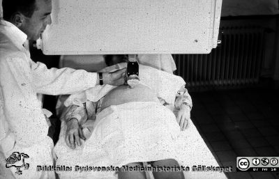 Bertil Sundén gör en ultraljudsundersökning på en gravid kvinna i början av 1960-talet
Bildkälla Bertil Sundén. Bilden finns publicerad i hans avhandling 1964. Apparaten var byggd i England, och Bertil Sundén började 1961 använda den. Den byggdes efter hans önskemål sedan han varit på studiebesök i England, och blev den enda i sitt slag. Firman fortsatte bygga ultraljudsapprater för industriellt bruk, inte medicinskt.
Nyckelord: Lasarett;Lund;Universitetssjukhus;USiL;Ultraljud;Kvinnoklinik;KK;Obstetrik