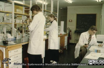 Forskning på distriktsläkarstationen i Dalby 1981
Ur låda med blandade diabilder från sjukhusfotograferna i Lund, 1970-, 1980- och 1990-talen. Läkarstationen i Dalby 810121. Forskn.assistenterna Marianne Béve-Nilsson till vänster och Elisabeth Elvander-Ståhl till höger Dr. Per-Olof Bitzén sittande vid bänken, doktorand.
Nyckelord: Lasarettet;Lund;Laboratorium;Universitet;Universitetssjukhus;USiL;Dalby;Läkarstation;Forskning