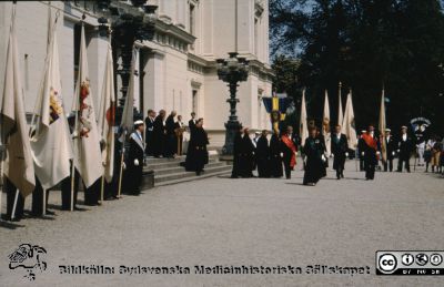 Promotionsprocession vid universitetshuset i Lund 1989
Doktorspromotion i Lund 1989. Övermarskalk Karin Dahlgren leder den akademiska processionen på väg ut ur universitetshuset. Marskalken längst till hö med rött band är Gunnar Pehrsson tidigare övermarskalk innan Karin tog över hela ansvaret 1985. Promotorerna har just kommit ned från universitetets trappa. En av dem, längst till höger i bild, kan var juristen Gunnar Bramstång, en annan kan vara Kjell Wallenius (odontologi), möjligen till vänster om honom kirurgen Stig Bengmark och på trappan till höger möjligen teknologen Sven-Gerhard Lindblad (LTH).  
Nyckelord: Doktor;Lund;Universitet;Procession;Doktorspromotion