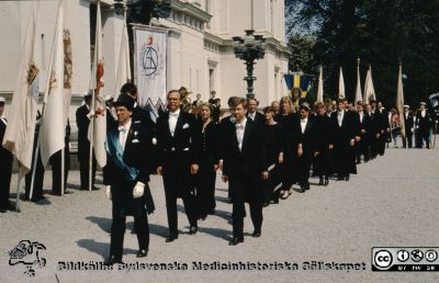 Promotionsprocession i Lund utanför universitetshuset 1989
Johan Wennerberg (öronläkare) som marskalk före medicinska fakultetens promovendi. Längst fram o delvis skymd av Johan finns Magnus Abrahamsson (klinisk kemist). Bredvid honom Morgan Andersson (öronläkare). Bakom Morgan ses Ellika Andolf (gynekolog) och bredvid henne enligt promotionsprogrammet Bengt Magnus Asking (skymd). Bakom Ellika skymtar hennes man Per Aspenberg (ortoped). Sedan ser vi Britt Beding Barnekow (oftalmolog), bakom henne till vä Hans Bergenudd (ortoped) och till höger den långa ljusa kvinnan som jag tror är Margareta Bramnert (endokrinolog). Bakom den mörke mannen som enligt promotionsprogrammet måste vara Tamal Mustapha Dakour syns Eva Degerman (medicinsk kemi) och bakom henne kanske Lars Edenbrandt (klinisk fysiologi)). 
Nyckelord: Lund;Universitet;Promotion;Procession