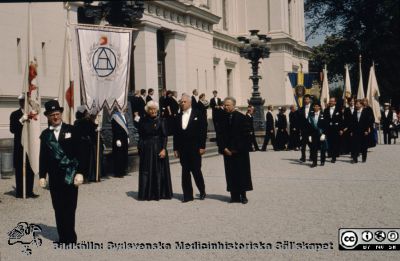 Processionen från universitetet vid doktorspromotion i Lund 1989. 
Marskalk Nils Dahlgren framför en trio blivande hedersdoktorer: landshövding Bertil Göransson i mitten. På hans högra sida Ingeborg Olsen-Hellberg, Malmö och på hans vänstra sida Seymour Schwarz, Rochester NY. I bakgrunden marskalken Johan Wennerberg framför medicinska fakultetens promovendi.
Nyckelord: Lund;Universitet;Promotion;Doktorspromotion;Procession;Hedersdoktor;Medicinska;Fakulteten