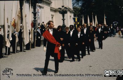 Processionen från universitetet vid doktorspromotion i Lund i slutet på 1980-talet 
Filosofiska fakultetens marslkalk med promovendi bakom.
Nyckelord: Doktor;Doktorspromotion;Procession;Universitet;Promotion;Lund;Filosofiska;Fakulteten