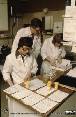 Forskning på distriktsläkarsttionen i Dalby 1981
Ur låda med blandade diabilder från sjukhusfotograferna i Lund, 1970-, 1980- och 1990-talen. Läkarstationen Dalby 810121, mottagningslaboratoriet med undersköterskan Ulla Rydell närmast och sjuksköterskan Eva Johannisson, som letar i pärmen medan dr. Per-Olof Bitzén står bakom, då doktorand.
Nyckelord: Distriktsläkare;Dalby;Universitet;Universitetsklinik;Lund;Laboratorium;Läkarstation