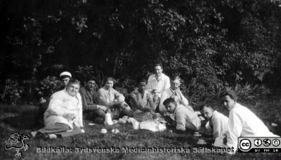Fotoalbum märkt Histologikursen Ht. 1927 på första bladet. 
Fotoalbum märkt Histologikursen Ht. -27 på första bladet. Det innehåller bilder från dåvarande histologiska avdelningen 
på anatomiska institutionen i Lund på Biskopsgatan 7. Bildtext "Laborationerna", men saknas i övrigt. Bilden visar studenter under en kaffepaus i parken vid institutionen. De har sina vanliga gångkläder medan lärare / amanuenser har vita laboratorierockar. Amanuensen längst till vänster är kanske Elvir Wahlbom (1907 - 1980), praktiserande läkare i Malmö från 1947. 
Bildkälla Stiftelsen Locus Medicus Lundensis 230317. Fotograf okänd.
Nyckelord: Histologiska avdelningen;Anatomiska Institutionen;Locus Medicus Lundensis;Medicinska fakulteten i Lund;Lärare;Amanuenser;Kaffe.