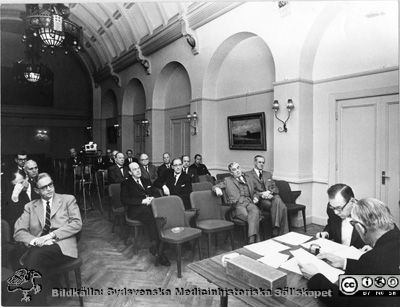 Sammanträde med Läkarsällskapet i Lund nära 1960.
Foto monterat på kartong. Påskrift: "Universitetet. Läkarsammankomster mm.". Sammanträde med Läkarsällskapet i Lund. Prof. Karl Emil Thulin sitter som sekreterare. Ordföranden är inte identifierad. Bland de främsta åhörarna ses från vänster Hjalmar Koch (föredragshållare), CG Ahlström, Alfred Flaum, Alf Sjövall och Nils Lindgren (öronläkare i Malmö). Snett bakom Alfred Flaum och till höger i bilden sitter Tord Gülich. Ytterligare ett steg åt höger sitter Anders Biörklund. Längre bak i salen syns urologen Lennart Andersson (glasögon, närmast väggen). Sammanträdeslokalen är Lilla Salen på Akademiska Föreningen. Tidpunkten bör vara något av åren runt 1960. Bilden lär finnas publicerad i Läkarsällskapet i Lund 100 år. 
Nyckelord: Läkarsällskapet;Lund;Sammanträde;Akademiska Föreningen