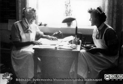 Sköterskor på urologiska kliniken i Lund i mitten på 1900-talet
Urologisk avdelning urologi låda A 3:2. Avdelningsföreståndaren under lång tid på urologiska kliniken i Lund i gamla kirurgibyggnaden,  Marta Ängeby (1908-2003), tillsammans med en yngre kollega. Arbetsbordet var nog inte större än så. Foto i mitten på 1900-talet.
Nyckelord: Lasarettet;Lund;Universitetssjukhuset;USiL;Urologisk;Kapsel 11;Kirurgisk;Klinik