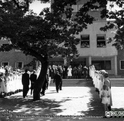 Konung Gustaf VI Adolf  besöker barnkliniken 1951
Rimligen från invigningen av barnkliniken i Lund 1951. Den vinkande mannen längst fram i processionen bör vara kung Gustaf VI Adolf. 
Från Thyra Åhlunds och Astrid Bjelks fotosamling skänkt till Radiologiska kliniken 10/4 1982. Thyra Åhlund (1907-1988) var sjuksköterska på radiologiska kliniken 1931-1942 och Astrid Bjelk från 1933 till sin pensionering.
Nyckelord: Lasarettet;Lund;Universitetssjukhuset;USiL;Barn;Pediatrisk;Klinik;Invigning