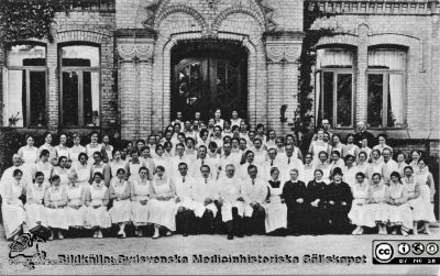 Professor Gustaf Petrén (1874-1962 med anställda på kirurgiska kliniken i Lund 1923. 
Kirurgiska kliniken, Lasarettet i Lund: Prof. Petrén med anställda 1923. Håkan Westling skrev 2010-07-25 " På Petréns hö sida troligen Nils Liedberg. Ovanför och till höger troligen Alf Sjövall och på hans vä sida Eric Millbourn". Anders Biörklund skrev 2020-12-05 "Läkaren, som står precis ovanför GP : kan det vara Sommar Bruzelius, som senare blev kirurgchef i Västerås?"
Per-Olof Mattsson i Lomma identifierade 2013 mannen i ljusa kläder längst till vänster i bilden som sin morfar, Jöns Christensson. Denne var sjukhustjänare eller vaktmästare från början av seklet till pensionen. Trol. sofiasyster Ebba Lagström som, nr 2 på bilden åt hö från Petrén. Efter tryckt vykort.
Nyckelord: Kirurgisk;Klinik;Lasarettet;Lund;Universitetssjukhus;Personal