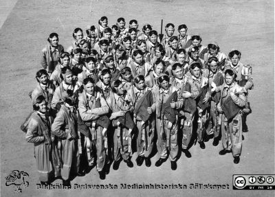 Fältflygarelever, flygofficersaspiranter, reservflygofficersaspiranter (bl. a Lars Malm vid pilen, sedermera professor i öron-näsa-halssjukdomar i Lund) samt på F5 i Ljungbyhed i slutet av maj 1954. 
Bilden visar officersaspiranter, reservofficersaspiranter (bl. a Lars Malm vid pilen, sedermera professor i öron-näsa-halssjukdomar i Lund) samt fältflygarelever när dei utexaminerades från F5 i Ljungbyhed i slutet av maj 1954. Ca 1000 pojkar sökte flygutbildning i fltgvapnet, 100 klarade inträdesproven och fick börja i juni 1953, hälften gallrades bort under flygutbildningen av olika skäl, fr.a. att man inte var bra på att flyga och det var knappt 50 som examinerades av flygvapenchefen general BG Nordenskjöld. Eleverna flög propellerplan på flygskolan. Sedan flög  reservarofficerselever jetplanet Vampire J28 på F18 i Tullinge och sedan Tunnan J29 på Barkarby i Stockholm. Lars Malm satte en Tunna i ett kärr, men flög 15 pass med J29 innan han hoppade av (ej ur) för att i stället utbilda sig till läkare. 
Bilden användes på en utställning på Livets Museum i Lund om fysiologiska institutionens berömda instrumentverkstad som Lars Malm ordnade.
Nyckelord: Fysiologisk;Institution;Lund;Universitet;Instrumentverkstad;Utställning