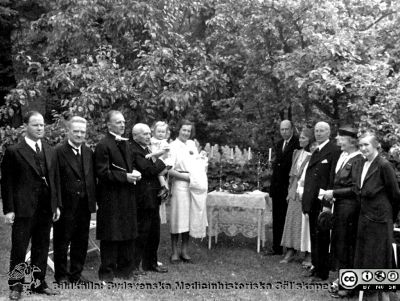 Barndop i familjen Essen-Möller 1941
Anders Essen-Möller döps 1941 av prosten i Dalby, Emil Lundblad,  i farfar Elis' trädgård på Finngatan 6. Denne står som nr 4 från vänster, med barnbarnet Kerstin i famnen. Signe står med den nydöpte Anders i gamnen. Till höger närmast dopbordet står Erik Essen-Möller och farmor Lisa. Publicerad på sid. 159 i Westling (2010). Bildkälla: Håkan Westling 2016.
Nyckelord: Barndop;Familj