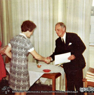 Professor Carl Gottfrid  Holmberg avtackar  okänd kvinna i mitten på 1900-talet
Bilder på A1-ark f. klin-kem jubileum 1997.	Gamla bilder	Professor Carl Gottfrid  Holmberg avtackar  okänd kvinna i mitten på 1900-talet.
Nyckelord: Laboratorium;Lasarettet;Lund;Klinisk;Kemi;Avdelningen;Universitetssjukhuset;USiL