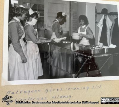 Bilder ur SSSH-sköterskan Anne-Marie Sörensens album från sin utbildning
"Matvagnen göres i ordning till patienternas middag".Tre unga kvinnor med elevmössor och ett vårdbiträde utan mössa men med enkel brosch på kragen.
Nyckelord: SSSH;Södra Sveriges Sjuksköterskehem;Lund;Elever