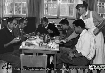  SSSH-sjuksköterskan Anne-Marie Sörensens bilder från sin utbildning och första tjänstgöringstid som legitimerad sjuksköterska
"Lunchen serverad för herrarna på sal B.". Sköterskan bär elevmössa. Bildkälla S. Anne-Marie Sörensen via S. Eva Ljunggren, SMHS.
Nyckelord: Lasarettet i Lund;Manlig vårdavdelning