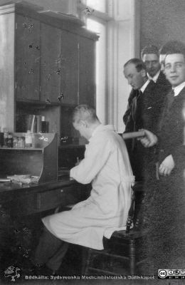 Album från histologikursen höstterminen 1925 i Lund
Album från histologikursen höstterminen 1925 i Lund. Bildtext: "Här skall läsas!"  Bilden visar ett antal studenter och troligen en amanuens i laboratorierock vid en bänk i kurslaboratoriet. Möjligen är nr 3 från höger av de stående Gösta Glimstedt (1905 - 1970), senare professor i histologi i Lund. Foto på histologiska avdelnigen i anatomiska institutionens hus på Biskopsgatan 7. Bildkälla Locus Medicus Lundensis 2025-03-17. Fotograf okänd.
Nyckelord: Histologiska avdelningen;Locus Medicus Lundensis;Medicinska fakulteten;Medicine studerande;Elever;Amanuenser;Anatomiska Institutionen;Kurslaboratorium