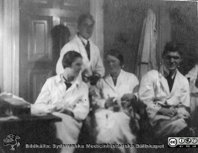Thesaurus histologiae 1926
Fotoalbum på första bladet märkt 
"Thesaurus histologiae. 
thet är 
Een obiektiv beskrifning aff hendelser på then histologiska skåådebanan A.D. MDMXXVI. Med tacksamhet och vördnad överräckt av Kurs och amanuenser.". 
Detta album innehåller bilder från histologiska avdelningen 
på anatomiska institutionen i Lund på Biskopsgatan 7. Bildtext: "Fig. 13. Husligt arbete."  Det ingick uppenbarligen i kursen att tvätta och torka objektsglas och andra glasvaror. Det var säkert ett utmärkt sätt att skapa samhörighet och trivsel på kursen. Foto i histologiska avdelningens kurslaboratorium på anatomiska institutionen.
Bildkälla Stiftelsen Locus Medicus Lundensis 250317. Fotograf okänd.
Nyckelord: Histologiska avdelningen;Locus Medicus Lundensis;Locus Medicus Lundensis;Medicinska fakulteten;Medicine studerande;Anatomiska Institutionen;Elever