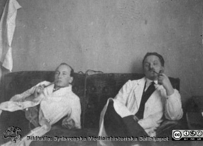 Thesaurus histologiae 1926
Fotoalbum på första bladet märkt "Thesaurus histologiae. 
thet är 
Een obiektiv beskrifning aff hendelser på then histologiska skåådebanan A.D. MDMXXVI. Med tacksamhet och vördnad överräckt av Kurs och amanuenser.". 
Detta album innehåller bilder från histologiska avdelningen 
på anatomiska institutionen i Lund på Biskopsgatan 7. Bildtext: "Fig. 15 Hederliga amanuenser (Hellman 1926)." Okänd amanuens till vänster, troligen Sture Siwe till höger. Foto i professorns soffa, kanske på hans arbetsrum i histologiska avdelningen på anatomiska institutionen.
Bildkälla Stiftelsen Locus Medicus Lundensis 250317. Fotograf okänd.
Nyckelord: Histologiska avdelningen;Locus Medicus Lundensis;Locus Medicus Lundensis;Medicinska fakulteten;Medicine studerande;Anatomiska Institutionen
