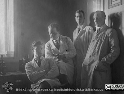 Thesaurus histologiae 1926
Fotoalbum på första bladet märkt 
"Thesaurus histologiae. 
thet är 
Een obiektiv beskrifning aff hendelser på then histologiska skåådebanan A.D. MDMXXVI. Med tacksamhet och vördnad överräckt av Kurs och amanuenser." på första bladet. 
Dett album innehåller bilder från histologiska avdelningen 
på anatomiska institutionen i Lund på Biskopsgatan 7. Bildtext: "Fig. 20 "Staben 1926." Troligast kursens amanuenser. Från vänster okänd, Sture Siwe (1897 - 1966; senare professor i pediatrik i Lund), okänd 2, Gösta Glimstedt (1905 - 1970; senare efterträdare till Torsten Hellman på professuren i histologi i Lund). Foto i mikroskopisalen på histologiska avdelningen på anatomiska institutionen.
Bildkälla Stiftelsen Locus Medicus Lundensis 250317. Fotograf okänd.
Nyckelord: Histologiska avdelningen;Locus Medicus Lundensis;Locus Medicus Lundensis;Medicinska fakulteten;Medicine studerande;Anatomiska Institutionen