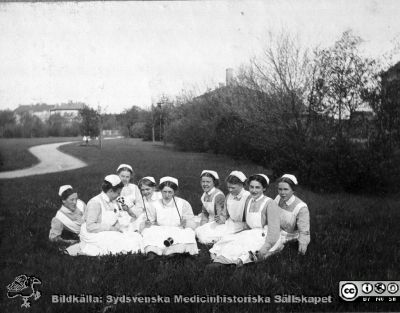 Eleverna på SSSH på utflykt i icke identifierad park. 
Bild 2 i husmor Anna Landelius (1880-1964) efterlämnade fotoalbum. Ingrid Frennhoff (f. 1944) hade övertagit detta album efter sin morfar som i sin tur tagit hand om det efter sin syster husmor Anna på Lasarettet i Lund. Gåva till Sydsvenska Medicinhistoriska Sällskapet nyåret 2020.
Ett par av eleverna har enkla utomhusleksaker med sig. Alla bär mössor, men ingen är färdig sjuksköterska med den karakteristiska SSSH-mössan. Några har bara enkla elevsnibbar.
Nyckelord: Husmor;Sjuksköterska;SSSH;Södra Sveriges Sjuksköterskehem;Utflykt;Park;Leksaker