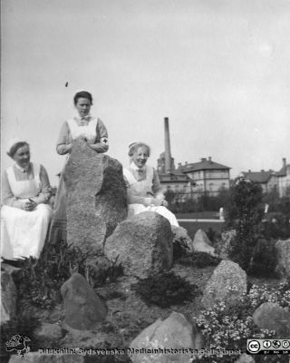 Tre sköterskor i ett stenparti, troligen vid Malmö Allmänna Sjukhus
Bild 11 i husmor Anna Landelius (1880-1964) efterlämnade fotoalbum. Ingrid Frennhoff (f. 1944) hade övertagit detta album efter sin morfar som i sin tur tagit hand om det efter sin syster husmor Anna på Lasarettet i Lund. Gåva till Sydsvenska Medicinhistoriska Sällskapet nyåret 2020.
- Tre sköterskor i ett stenparti i en park med troligen panncentralen och en vårdbyggnad på ett sjukhus i bakgrunden. Foto möjligen vid Malmö Allmänna Sjukhus. Kvinnan till vänster  bär varken sköterskebrosch eller SSSH-mössa. Kan möjligen vara Anna Landelius under hennes elevtid. Kvinnan i mitten är kanske en dansk sköterska med mössa och hakband eller möjligen en Röda Kors-sköterska. Hon till höger är en SSSH-sjuksköterska med mössa, hakband och brosch.
Nyckelord: Sjuksköterska;SSSH;Södra Sveriges Sjuksköterskehem;Malmö Allmänna Sjukhus