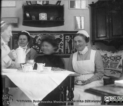 Kaffekalas med tre kvinnor i sköterskeuniform. 
Bild 13 i husmor Anna Landelius (1880-1964) efterlämnade fotoalbum. Ingrid Frennhoff (f. 1944) hade övertagit detta album efter sin morfar som i sin tur tagit hand om det efter sin syster husmor Anna på Lasarettet i Lund. Gåva till Sydsvenska Medicinhistoriska Sällskapet nyåret 2020.- Kvinnan till vänster med kaffekanna bär SSSH-mössa. Kvinnan till höger bär elevsnibb och kan vara Anna Landelius. Kvinnan bortom kaffekannan har sjuksköterskemössa med hakband.
Nyckelord: Sjuksköterska;SSSH;Södra Sveriges Sjuksköterskehem;Kaffekalas