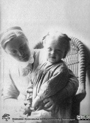 Ung SSSH-sköterska, möjligen Anna Landelius, 
Bild 50 i husmor Anna Landelius (1880-1964) efterlämnade fotoalbum.Ingrid Frennhoff (f. 1944) hade övertagit detta album efter sin morfar som i sin tur tagit hand om det efter sin syster husmor Anna på Lasarettet i Lund. Detta album är en gåva från Ingrid Frennhoff  till Sydsvenska Medicinhistoriska Sällskapet nyåret 2020.
Sköterskan sitter i korgstol med ett barn i sitt knä. Samma fototillfälle som bilden i fil AL_LA2020-049Cpg.jpg
Nyckelord: Sjuksköterskor;SSSH;Barn