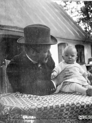 Medelålders man med liten pojke på lantgård. 
Bild 75 i husmor Anna Landelius (1880-1964) efterlämnade fotoalbum. Ingrid Frennhoff (f. 1944) hade övertagit detta album efter sin morfar som i sin tur tagit hand om det efter sin syster husmor Anna på Lasarettet i Lund. Detta album är en gåva från Ingrid Frennhoff till Sydsvenska Medicinhistoriska Sällskapet nyåret 2020.
Kanske på Anna Landelius fädernegård Jakobslund i Ljungsbro?
Nyckelord: Lantgård;Barn;Spädbarn