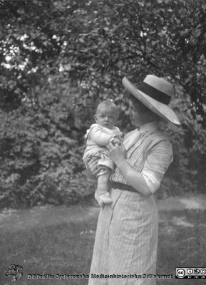 Kvinna med liten pojke på lantgård. 
Bild 76 i husmor Anna Landelius (1880-1964) efterlämnade fotoalbum. Ingrid Frennhoff (f. 1944) hade övertagit detta album efter sin morfar som i sin tur tagit hand om det efter sin syster husmor Anna på Lasarettet i Lund. Detta album är en gåva från Ingrid Frennhoff till Sydsvenska Medicinhistoriska Sällskapet nyåret 2020.
Kanske på Anna Landeliusm fädernegård Jakobslund i Ljungsbro? Den stora hatten talar för att bilden är tagen under 1900-talets första decennium.
Nyckelord: Barn;Spädbarn;Lantgård