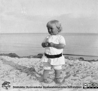 Litet barn på sandstrand vid öppen kust. 
Bild 81 i husmor Anna Landelius (1880-1964) efterlämnade fotoalbum. Ingrid Frennhoff (f. 1944) hade övertagit detta album efter sin morfar som i sin tur tagit hand om det efter sin syster husmor Anna på Lasarettet i Lund. Detta album är en gåva från Ingrid Frennhoff till Sydsvenska Medicinhistoriska Sällskapet nyåret 2020.
Rimligen ett syskonbarn till Anna Landelius. Falsterbo?
Nyckelord: Barn;Sandstrand