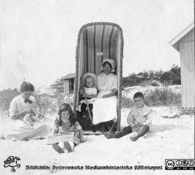 Kvinnor och barn på badstrand med strandtält, solstol och badhytter
Bild 88 i husmor Anna Landelius (1880-1964) efterlämnade fotoalbum. Ingrid Frennhoff (f. 1944) hade övertagit detta album efter sin morfar som i sin tur tagit hand om det efter sin syster husmor Anna på Lasarettet i Lund. Detta album är en gåva från Ingrid Frennhoff till Sydsvenska Medicinhistoriska Sällskapet nyåret 2020.
 Rimligen anhöriga till Anna Landelius. Falsterbo?
Nyckelord: Badstrand;Familj;Badtält;Badhytter;Solhytter