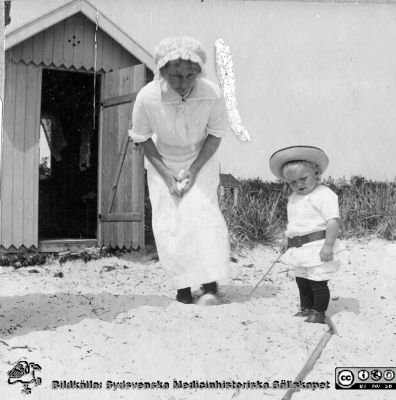 Kvinna med barn på sandstrand, troligen vid Falsterbohus
Bild 89 i husmor Anna Landelius (1880-1964) efterlämnade fotoalbum. Ingrid Frennhoff (f. 1944) hade övertagit detta album efter sin morfar som i sin tur tagit hand om det efter sin syster husmor Anna på Lasarettet i Lund. Detta album är en gåva från Ingrid Frennhoff till Sydsvenska Medicinhistoriska Sällskapet nyåret 2020.Ang
Rimligen anhöriga till Anna Landelius.
Nyckelord: Barn;Sandstrand;Badstrand;Badhytt