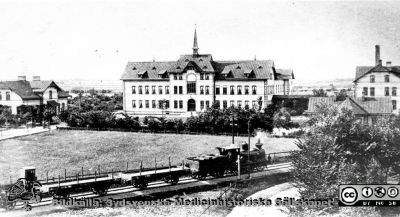 Reprofoto av rastrerad bild av Malmö Allmänna Sjukhus med järnvägsspåret Malmö-Ystad framför och ett godståg draget av ett ånglok.
 Foto nära sekelskiftet 1900.
Foto från samling funnen på KK i Lund hösten 2016 och tillvaratagen av en sekreterare där i samband med att hon gick i pension och överlämnat den till Sydsvenska Medicinhistoriska Sällskapet utan att ange sitt namn. 
Nyckelord: Malmö;MAS;Allmänna;Sjukhus;Fasad;Exteriör;Järnväg;nglok
