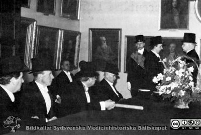 Doktorsutnämning i medicinska fakulteten i Lund 1935.
Doktorsutnämning i medicinska fakulteten i Lund 1935 i fakultetsrummet. Erik Ask-Upmark harangerar professor Otto af Klercker. Marskalken med bandet i bakgrunden är Otto Östberg, senare överläkare på medicinska kliniken i Växjö. Vid bordet sitter från vänster professorerna Axel Westman (gynekolog), Henrik Sjöbring (psykiatriker), Erik Widmark (medicinsk kemi) och Elis Essen-Möller (obstetrik och gynekologi). Hans Hellmer (röntgenolog)  sitter bakom, med ryggen mot väggen.
Nyckelord: Medicinsk fakultet;Medicinska fakulteten i Lund;Examen;Högtid;Sammanträde