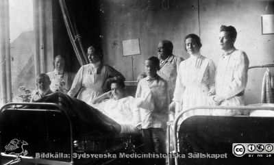  Ängelholms sjukhus. Lasarettsläkare Carl Adlercreutz på en sjuksal med sköterskor och patienter.
Efter diabild i sjuksköterskan Lillie Börjessons  samling från Ängelholms sjukhus. Lasarettsläkare Carl Adlercreutz på en sjuksal med sköterskor och patienter. Adlercreutz står i bildens centrum, nr 3 från höger. Han är helt vithårig, och bilden bör därmed vara tagen efter 1916, då han porträtterades så.
Nyckelord: Lasarett;Lasarettsläkare;Patienter;Personal;Engelholm;Ängelholm;Sjukhus;Vårdsalar