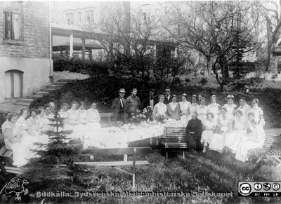 Ängelholms sjukhus. Ett kalas i sjukhusparken. 
Efter diabild i sjuksköterskan Lillie Börjessons  samling från Ängelholms sjukhus. Personalfest i sjukhusparken 1925. Rimligen lasarettsläkare Carl Adlercreutz i bildens mitt i hatt med ljust hattband, mustasch, skägg och slips. I andra raden längst ut till höger ses nattsköterskan Anna Lundström, av alla känd som "Anna Natt". Hon tjänstgjorde 1925 - 1956.
Nyckelord: Engelholm;Ängelholm;Sjukhus;Kalas;Sjukhusparken