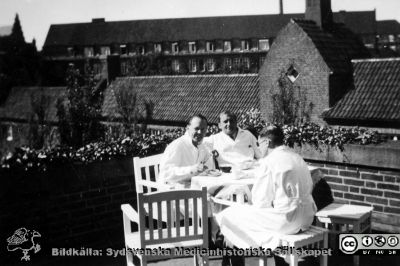 Kaffepaus på altanen till röntgenavdelningen på Lasarettet i Lund på 1930-talet.
Tre läkare tar kaffepaus på altanen i nordvästra hörnet av administrations- och röntgenbyggnaden på Lasarettet i Lund vid Allhelgona Kyrkogata. Den ovanjordiska kulverten mellan det gamla södra lasarettsområdet i kvarteret Paradis och det nya norra ses på andra sidan kyrkogatan. Dåvarande kvinnokliniken bildar fond. År 2020 är den nu Rehabhuset. De tre läkarna är inte identifierade. Möjligen kan det vara Inge Gynning längst till vänster? Denne blev så småningom radiolog i Malmö. Foto rimligen på 1930-talet. Från Syster Elinas fotoalbum (Elina Holmberg?).
Nyckelord: Röntgenologi;Lasarettet i Lund;Universitetssjukhus