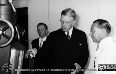 Kungligt besök på radiologiska kliniken i Lund 1951. 
Kung Gustaf VI Adolf besöker radiologiska kliniken i Lund 1951 för att bese och kanske inviga Kurt Lidéns s.k. koboltkanon. Här ses kungen vid koboltkanonen tillsammans med en hovman och klinikchefen Bertil Ebenius i vit rock. Från Syster Elinas fotoalbum (Elina Holmberg?).
Nyckelord: Koboltkanon;Radiologisk;Onkologisk;Jubileumsklinik;Strålbehandling;Lunds lasarett;Invigning