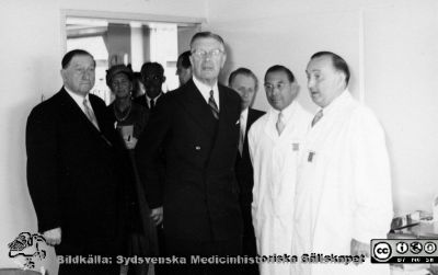 Kungligt besök på radiologiska kliniken i Lund 1951. 
Kung Gustaf VI Adolf på besök på radiologiska kliniken i Lund1951 då Kurt Lidéns s.k. koboltkanon demonstrerades för honom. Oidentifierad landstingspolitiker längst till vänster. Klinikchefen docent Bertil Ebenius till höger om kungen och docent Gunnar Gorton längst till höger i bilden. I bakgrunden personer ur kungens stab. Från Syster Elinas fotoalbum (Elina Holmberg?).
Nyckelord: Radiologisk;Klinik;Onkologisk;Jubileumsklinik