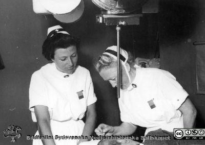 Två SSSH-sjuksköterskor ställer in strålbehandling 
Två SSSH-sjuksköterskor ställer in strålbehandling på en patient på radiologiska kliniken i Lund, troligen på 1950-talet.
Nyckelord: Radiologisk;Klinik;Lasarettet i Lund;Strålbehandling;SSSH;Sjuksköterska