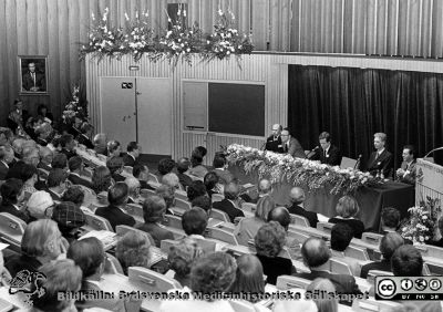 Forskningens Dag 1983 i Lund
Lasarettsfotograferna i Lund,  pärm  Sv/v Neg, 83:2. Forskningens Dag 1983 i Lund: "Cancerforskning - en nyckel til liv". Omärkt bild. I panelen, från vänster: professorerna Lars-Åke Fransson, Hans-Olof Sjögren, Dick Killander, Inge Olsson och Felix Mitelman. Sveriges kungapar, Drottning Siliva och kung Carl XVI Gustaf sitter främst i publiken. Från foto.
Nyckelord: Lasarettet;Lund;Universitetssjukhuset;USiL;Forskningens Dag;Cancer