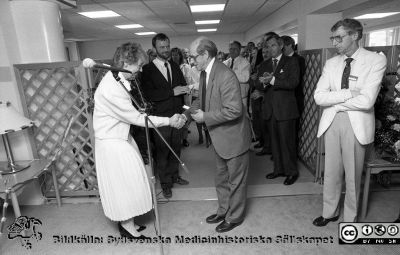 Patienthotellet invigs, troligen 1988
Lasarettsfotograferna i Lund.  Blandade negativ, omärkta år 1988-1995 (lösa negativhållare). 88-05-05, A.  Sjukhusdirektionens ordförande Fredrik Swartling skakar hand med kanslidirektören på Fernströmstiftelsen och gideoniten Ingegärd Lindqvist som just överlämnat biblar till hotellet och en också till Fredrik Swartling. Samfundet gideoniterna spred biblar i samhället i stort, bl.a. på sjukhuset. Bakom dem i mörk kostym och skägg kanske administratören Nils Topphem. Från negativ.
Nyckelord: Lasarettet;Lund;Universitetssjukhuset;USiL;Patienthotell