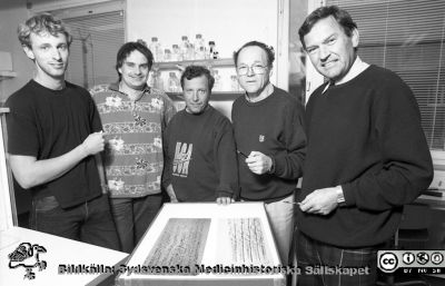 En grupp biomedicinska forskare
Lasarettsfotograferna i Lund.  Blandade negativ, omärkta år 1988-1995 (lösa negativhållare). Näst längst till höger troligen prof. Hans-Olof Sjögren och längst till höger docent (senare professor) Leif Salford. Pappren på bordet visar troligen en molekylärgenetisk analys. Foto 92-10-21.	Från negativ.
Nyckelord: Lasarettet;Lund;Universitetssjukhuset;USiL;Neurokirirugisk;Klinik