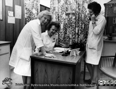I expeditionen på infektionsklinikens mottagning i Lund
Foto ur ett album tillägnat professor Karl Emil Thulin på hans 60-årsdag, 1975. Från vänster sekreterare / receptionist fru Brita Jäderström (hon var klinikens vänlighet utåt), Syster Anna-Greta Martinsson (avdelningsföreståndare på mottagningen; sittande) och institutionssekreterare Gun Mårtensson med telefonlur.
Nyckelord: Lasarettet;Lund;Universitetssjukhuset;USiL;Infektion;Kliniken;Epidemiologiska