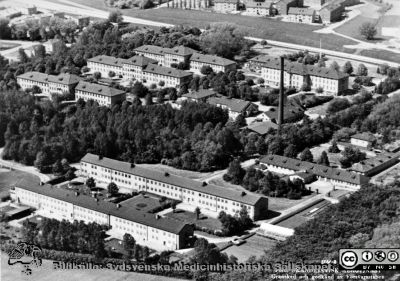 Vipeholms sjukhus. Flygfoto från efter mitten på 1950-talet
Från kurator Kerstin Löfströms (1928-1992) bildsamling från Vipeholms sjukhus i Lund, 1970 - 1980-talen och deponerad 2015-07-15 hos Sydsvenska Medicinhistoriska Sällskapet av dottern Ingrid Löfström i Lund.
Kerstin Löfström hade i många år sitt kontor  i administrationsbyggnaden bortom alla de gamla kasernerna, inte långt från motorvägen. Hennes dotter Ingrid skriver 2016:  
"I de tre  byggnaderna till vänster bodde patienter. I det lilla låga, lite mörkare huset närmast motorvägen var det kontor/administration. Som kurator hade min mor, Kerstin Löfström, under alla år kontorsrum i byggnaden närmast motorvägen" 
och
"Ungefär mitt i bilden syns några lägre hus, delvis skymda av träd. Där var det en samlingslokal och en välbesökt kiosk ( i alla fall fr om andra halvan av 70-talet)."
Flygfoto från efter mitten på 1950-talet då motorvägen byggdes.
Nyckelord: Mentalsjukhus;Psykiatrisk;Klinik;Vårdhem;Vipeholmsanstalten