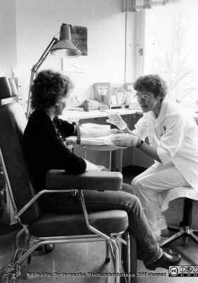 Sjukhusets företagshälsovård i Lund. 
Bildkälla avdelningsföreståndaren, sjuksköterkan Eva Ljunggren när hon tar hand om en patient. 4-5/84, foto/AV. Från originalfoto.
Nyckelord: Lasarettet;Lund;Universitetssjukhuset;USiL;Företagshälsovård