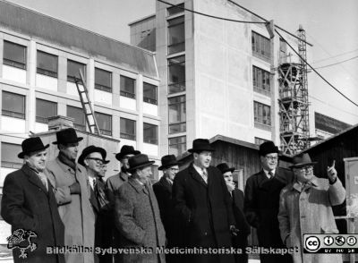 Inrikesministern med följe inspekterar 1958 byggarbetsplatsen för centralblocket i Lund
Omonterat fotografi märkt "Besök av inrikesminister Rune Johansson den 17/3 -58" från lasarettsdirektörens kontor, i mapp med påskrift "Fotoarkiv. Byggnadsarbeten för C-blocket". Nr 1 från vänster är Rune Johansson, nr 2 från vä är prof. Olle Olsson. Nr 6 från vä är landstingsmannen Torsten Andrée. Nr 7 från vänster är sjukhusdir. Arne Johansson. Mannen längst till höger, i ljus rock och med höjt pekfinger, är arkitekten, Stephan Hornyánszky. AB-blocket i bakgrunden är ännu inte riktigt klart (vilket det blev 1959).
Nyckelord: Kapsel 26;Bygge;Lasarettet;Lund;Regering;Landsting;Blocket;1950-talet;Centralblocket