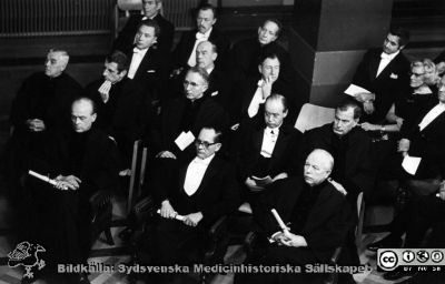 Professorsinstallation i Lunds Universitets aula.
Professorsinstallation i aulan vid Lunds universitet i mitten av 1960-talt. I främre raden från vänster Bengt Falck, NN Berglund?, Lars Philip Bengtsson. I andra raden från vänster Alf Sjövall?, Bengt Borgström, Nils Alwall, Carl Herman Hjortsjö, Gunnar L...?`. I tredje raden Stephen Thesleff, Carl Gustaf Ahlström, Ragnar Müller. I fjärde raden från vänster Olle Olsson, Sten Lagerstedt och okänd. I bildens högra kant Inga Marie Nilsson. Okänd fotograf.
Nyckelord: Professorsinstallation;Universitetet i Lund;Aula