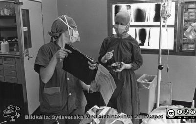 På en operationssal på lasarettet i Lund
Brun ringbunden mjuk pärm, kirurgiska kliniken i Lund. På en operationssal. En osteril assistent visar upp patientens journal för den ansvariga sterilklädda operationssköterskan. Foto, monterat.
Nyckelord: Lasarettet;Lund;Universitetssjukhuset;USiL;Operationsavdelningen;Kirurgiska;Kliniken